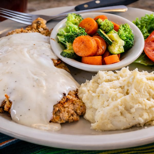 Chicken fried steak with gravy, mashed potatoes, and a side of mixed vegetables.