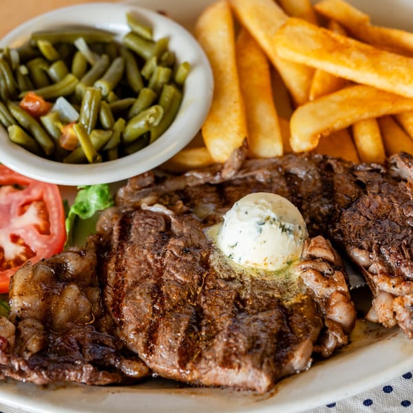 Grilled steak with melting butter, a side of french fries, green beans, and sliced tomatoes.