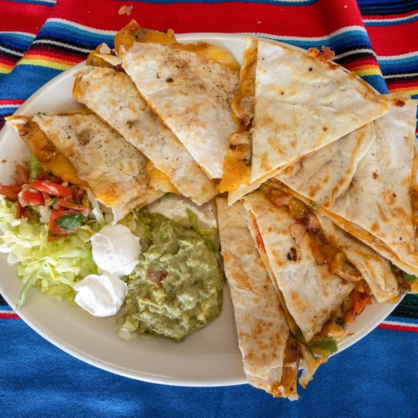 A plate of cheesy quesadilla wedges with guacamole, sour cream, and pico de gallo.