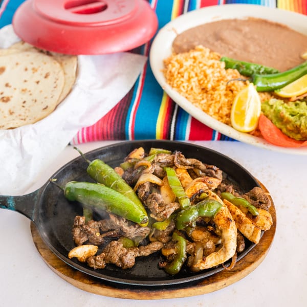 Sizzling beef and chicken fajitas with peppers and onions, served with tortillas, rice, beans, and guacamole.