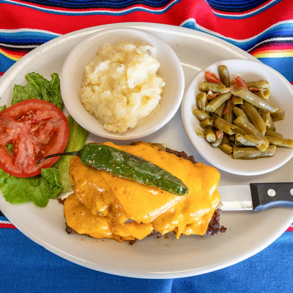 A Tex-Mex chopped steak with melted cheese and a green chili, served with mashed potatoes and green beans.