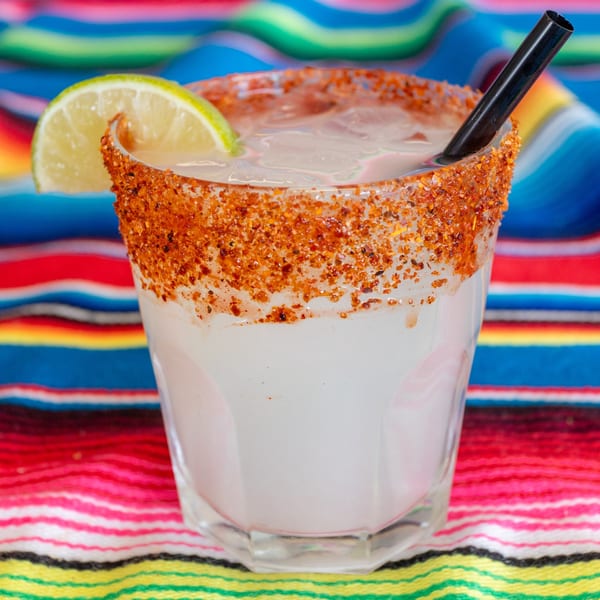 A Town House Restaurant margarita with a chili-lime rim, lime wedge, and black straw on a colorful striped blanket.