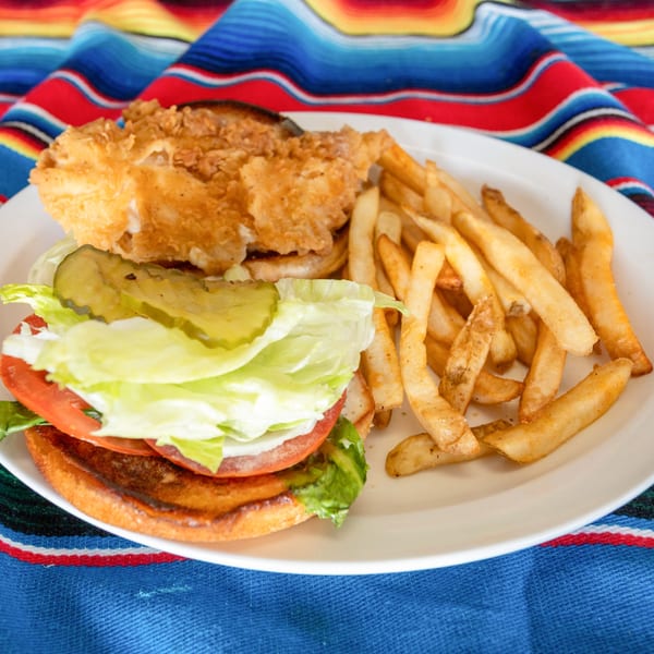 Crispy fried chicken sandwich with lettuce, tomato, and pickles, served with french fries on a white plate.