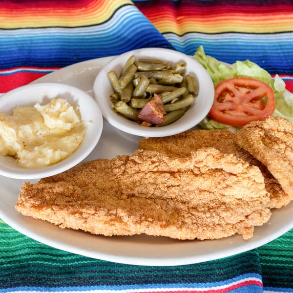 Fried catfish with mashed potatoes, green beans, lettuce, and tomato on a colorful striped tablecloth.