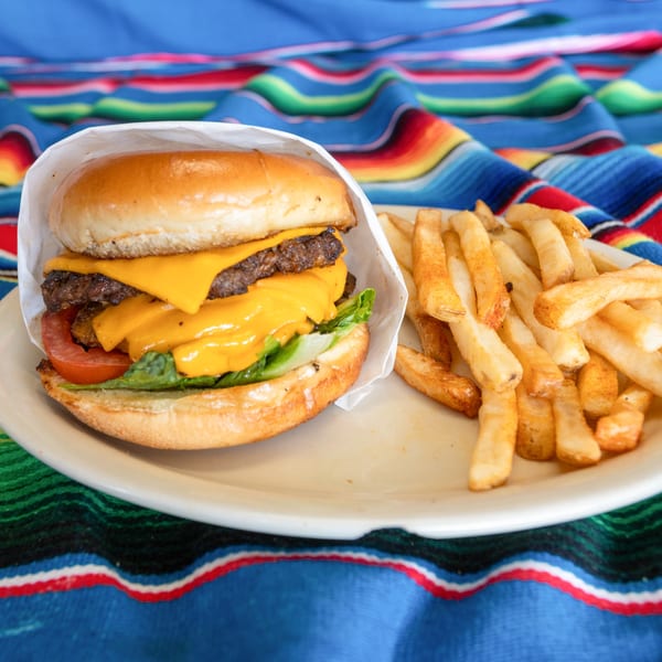 A double cheeseburger with lettuce and tomato, served with a side of fries on a colorful striped blanket.