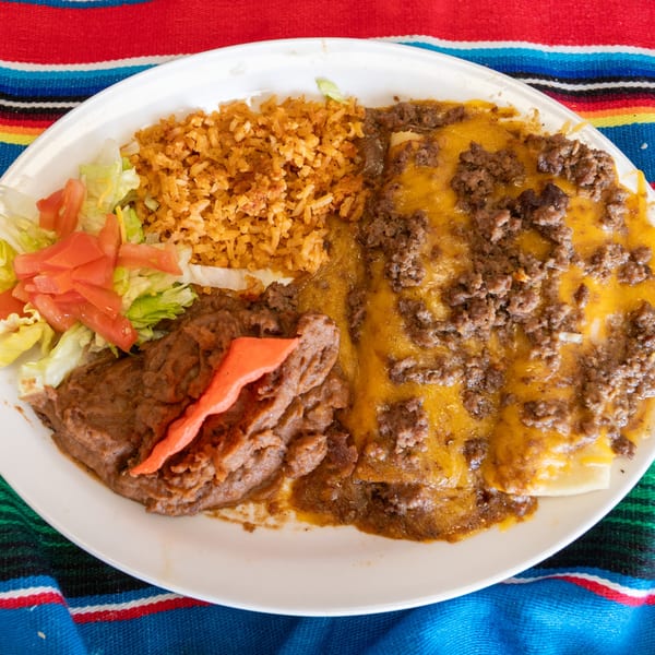 A Tex-Mex platter with enchiladas, rice, refried beans, and a side salad on a colorful striped tablecloth.